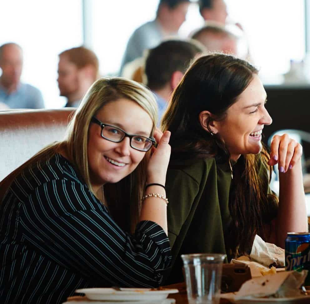 Two women smiling together in a booth at a casual restaurant or bar