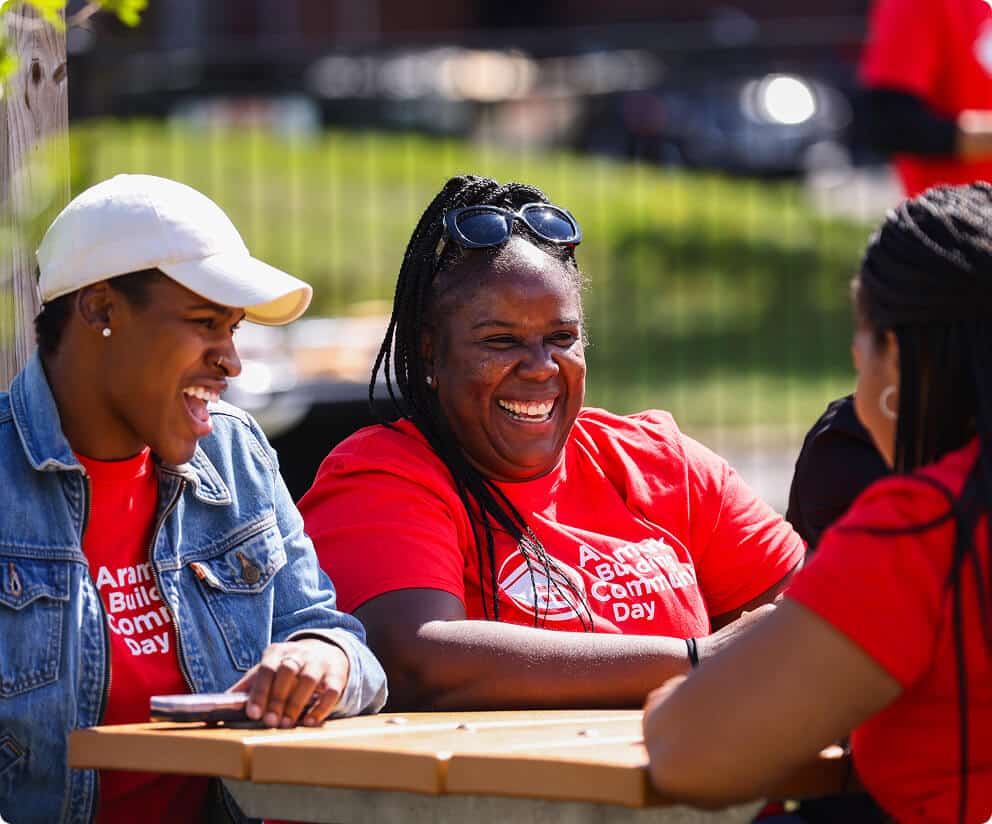 Employees in "Aramark Building Community Day" T-shirts laughing together at an outdoor picnic table